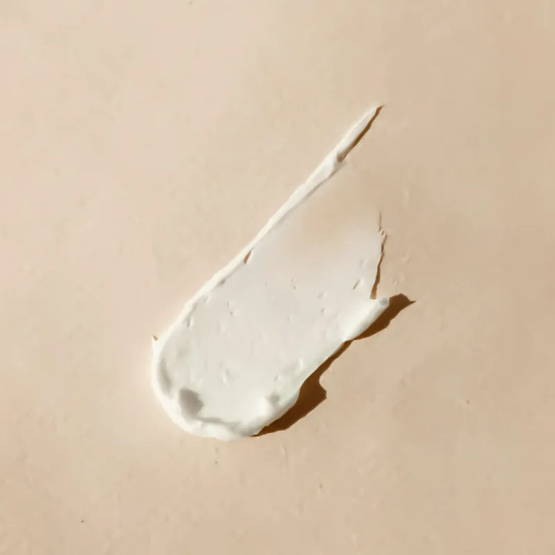 Crema blanca extendida sobre una superficie cálida, con sombra dura